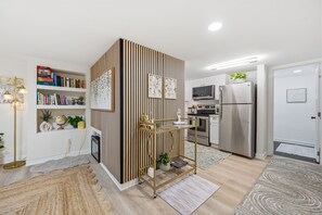 Una cocina moderna con electrodomésticos de acero inoxidable, un panel de madera decorativo y una estantería con libros y objetos decorativos.