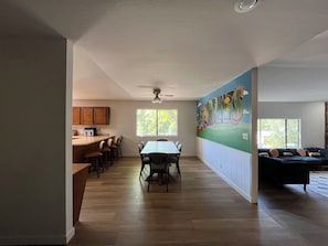 A spacious living area with a dining table, kitchen, and a mural on the wall.