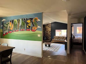 A room with a Murphy's Hotel mural, a stone fireplace, a sofa, and a dining area.