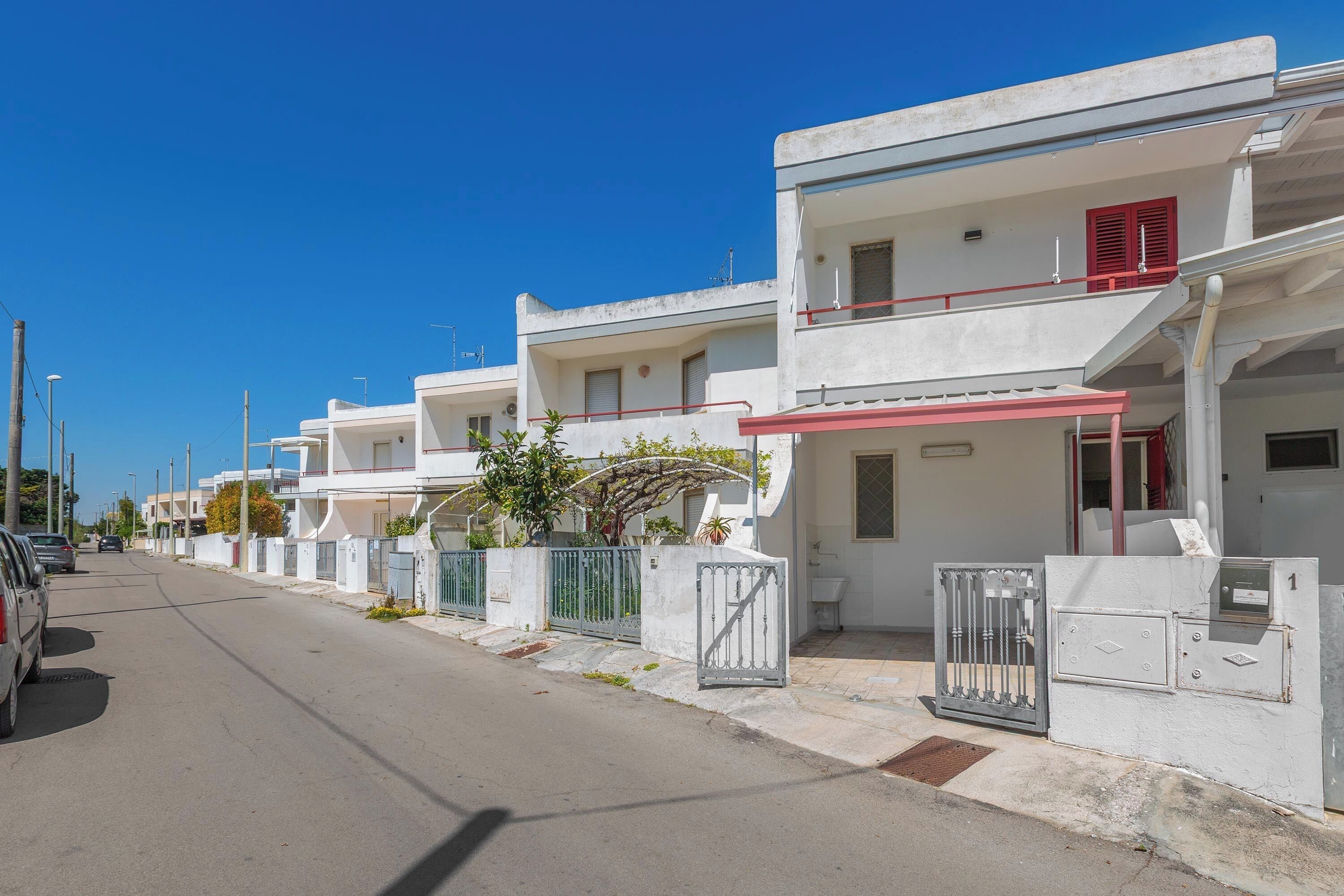 A row of white buildings with balconies, a gated entrance, and a clear sky.