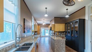 A kitchen with a marble countertop, stainless steel sinks, a black refrigerator, and a ceiling fan.