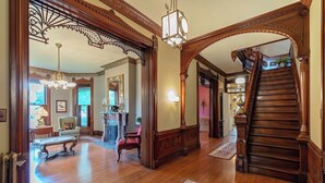 A grand foyer with a wooden staircase, ornate woodwork, and a chandelier.