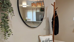 Ein Zimmer mit einem runden Spiegel, einer Bank mit Kissen, einem Kleiderhaken und einer hängenden Pflanze.