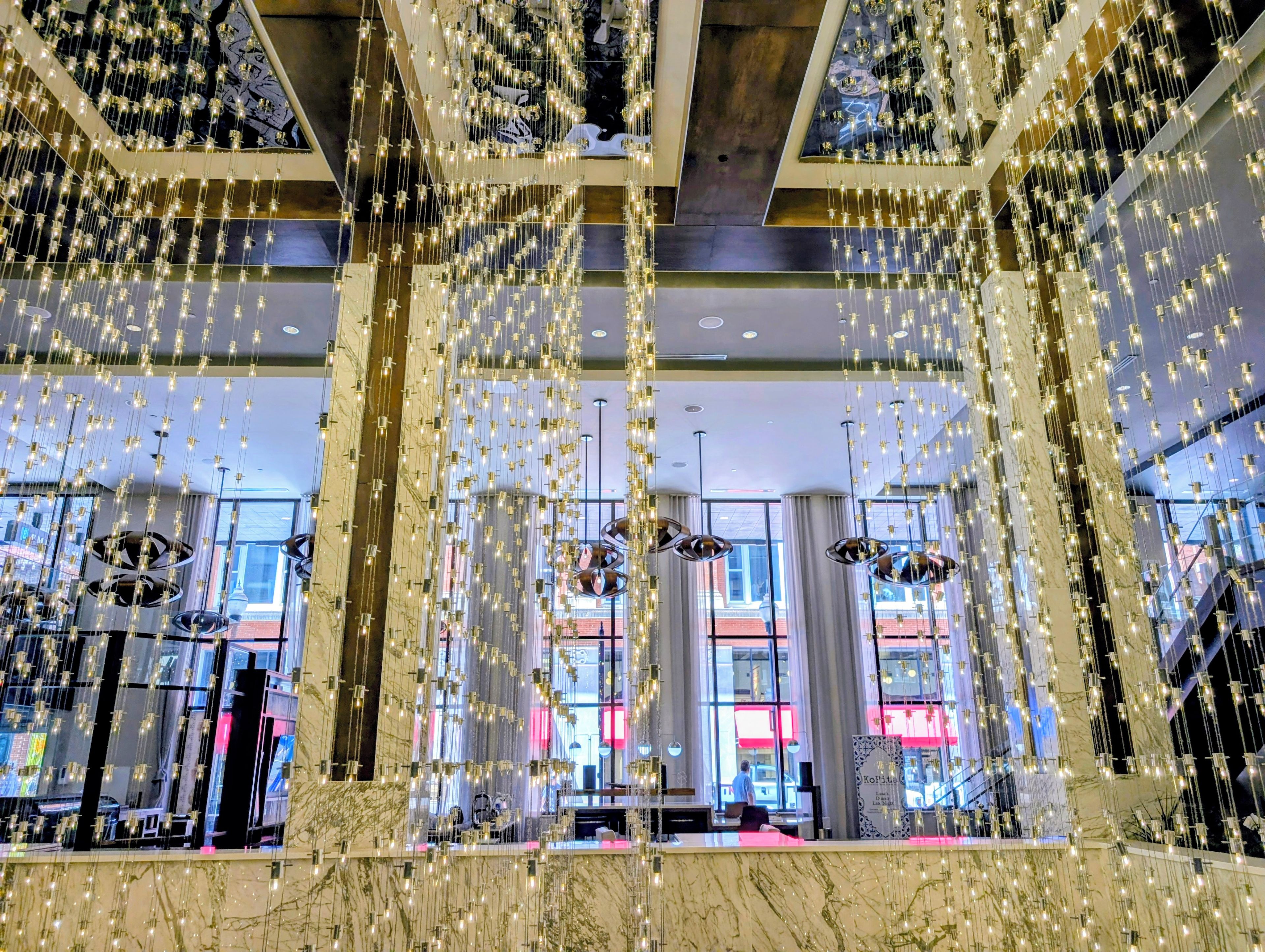 Un vestíbulo de hotel con columnas de mármol, lámparas colgantes y amplios ventanales.