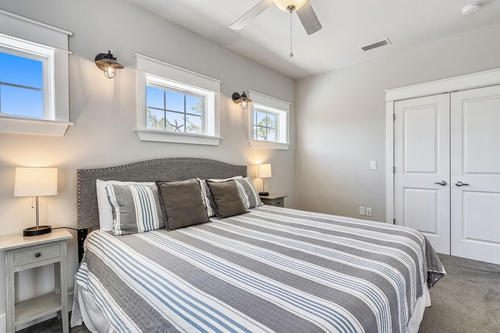A bedroom with a bed, two bedside lamps, a ceiling fan, and a door.