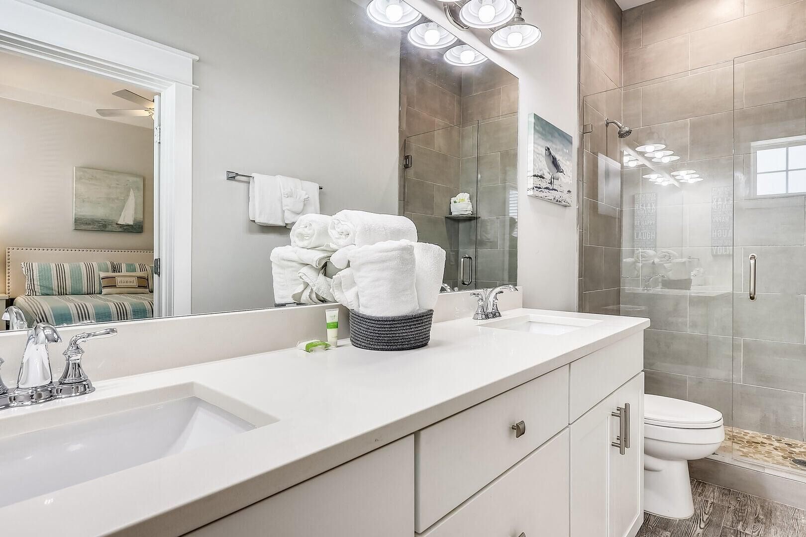 A modern bathroom with a large mirror, two sinks, a toilet, and a shower.