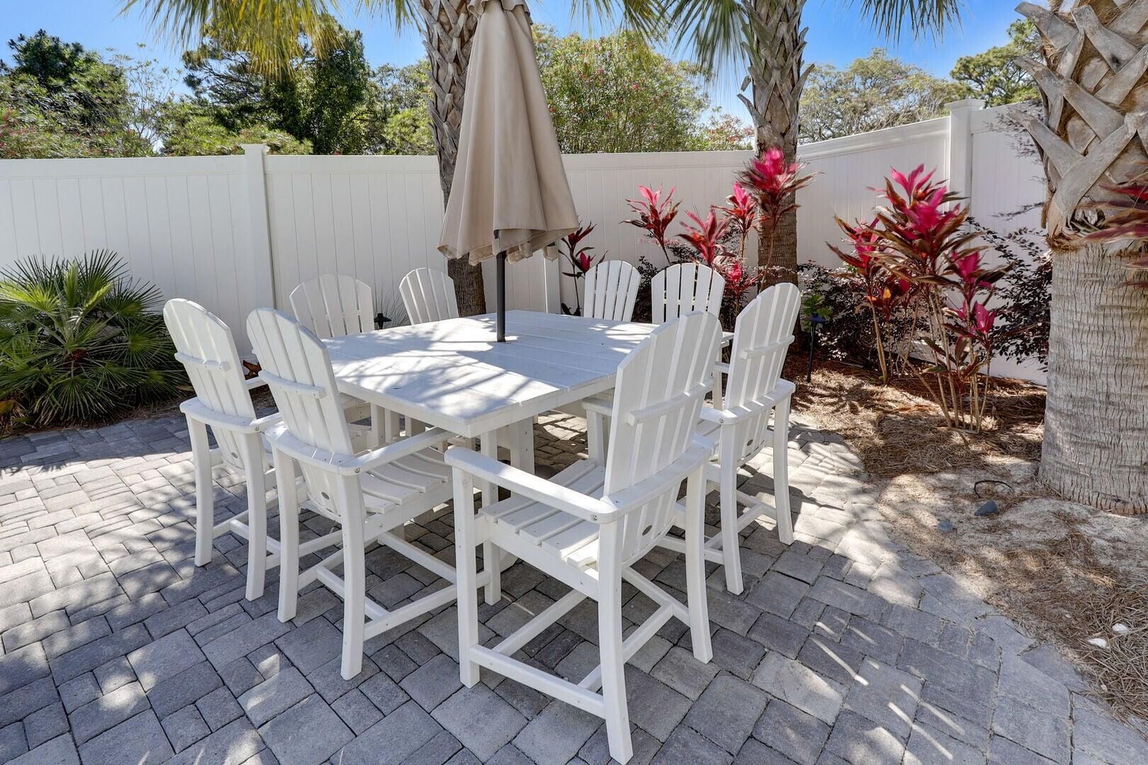 Une terrasse avec une table et des chaises blanches, entourée de plantes et d’une clôture blanche.