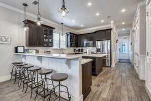 A modern kitchen with dark cabinetry, a central island with stools, stainless steel appliances, and pendant lighting. - Salty Shores (Miramar Beach)