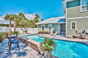 A pool area with a patio, chairs, and a house in the background. - Salty Shores (Miramar Beach)