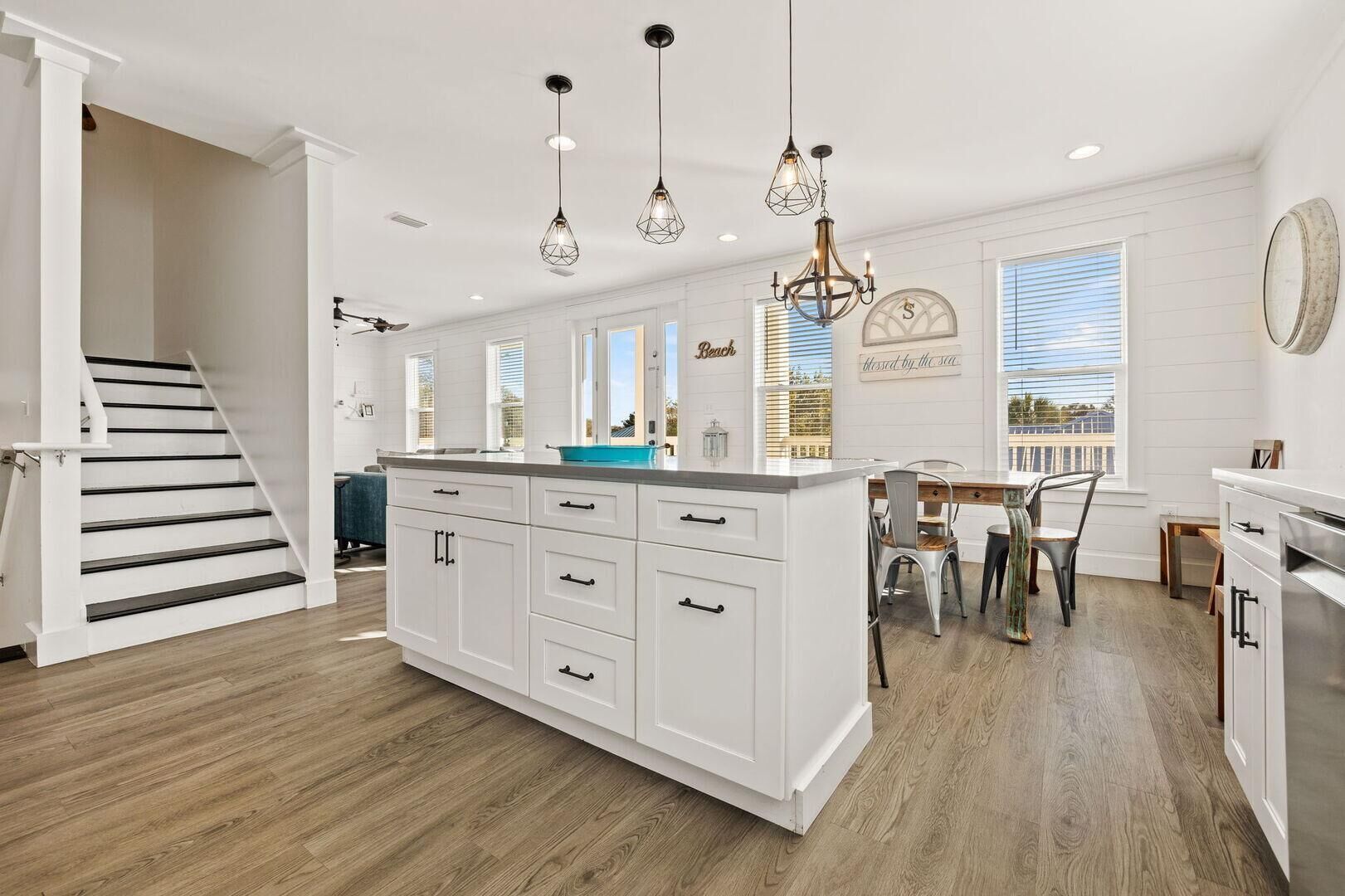 A modern kitchen with white cabinetry, a central island, pendant lighting, and a dining area with a view of the sea.