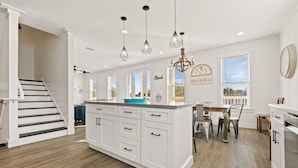 A modern kitchen with white cabinetry, a central island, pendant lighting, and a dining area with a view of the sea. - Sealah @ Crystal Beach (Destin)