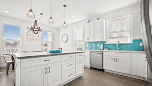 A modern kitchen with white cabinetry, a large island, and a blue backsplash. - Sealah @ Crystal Beach (Destin)