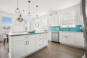 A modern kitchen with white cabinetry, a large island, and a blue backsplash. - Sealah @ Crystal Beach (Destin)