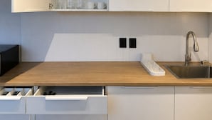 Cozinha moderna com armários brancos, bancada de madeira, pia de aço inoxidável e lava-louças embutida.