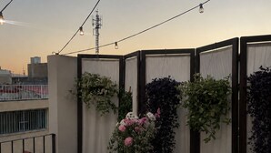Uma varanda com uma mesa redonda, duas cadeiras, um arranjo de flores e vista para a cidade.