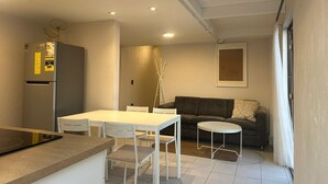 Um espaço de estar compacto com cozinha compacta, uma mesa de jantar com cadeiras, um sofá e uma pequena mesa lateral.