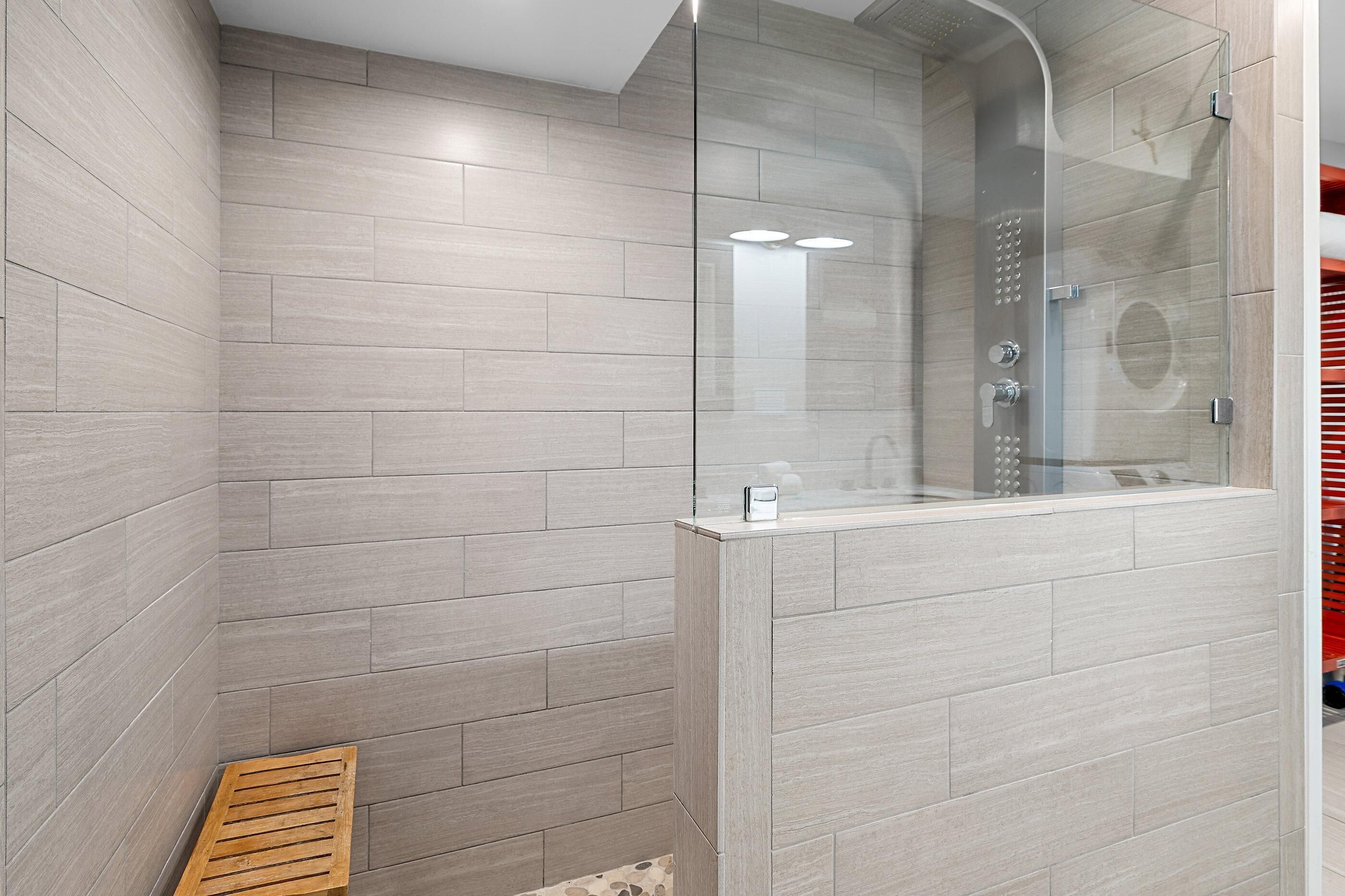 A modern shower enclosure with a glass door, a wooden bench, and a tiled wall.