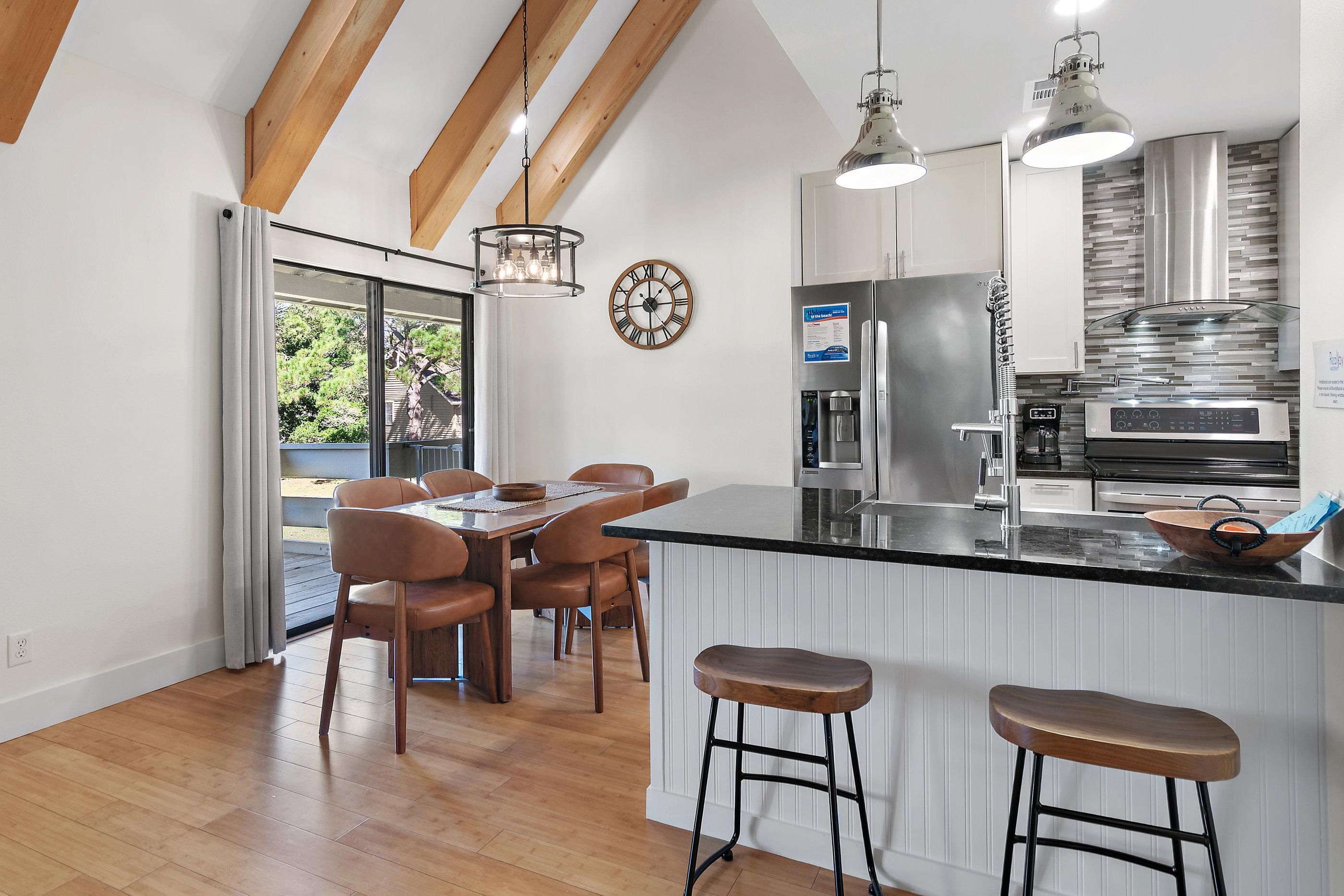 A modern kitchen with a large island, bar stools, and a dining area with a wooden table and chairs.