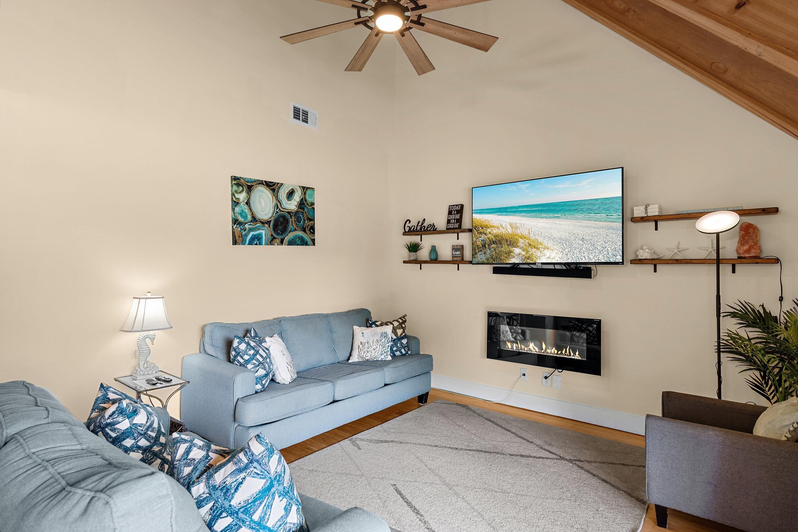 A living room with a blue sofa, a fireplace, a television, and a ceiling fan.