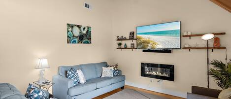 A living room with a blue sofa, a fireplace, a television, and a ceiling fan.