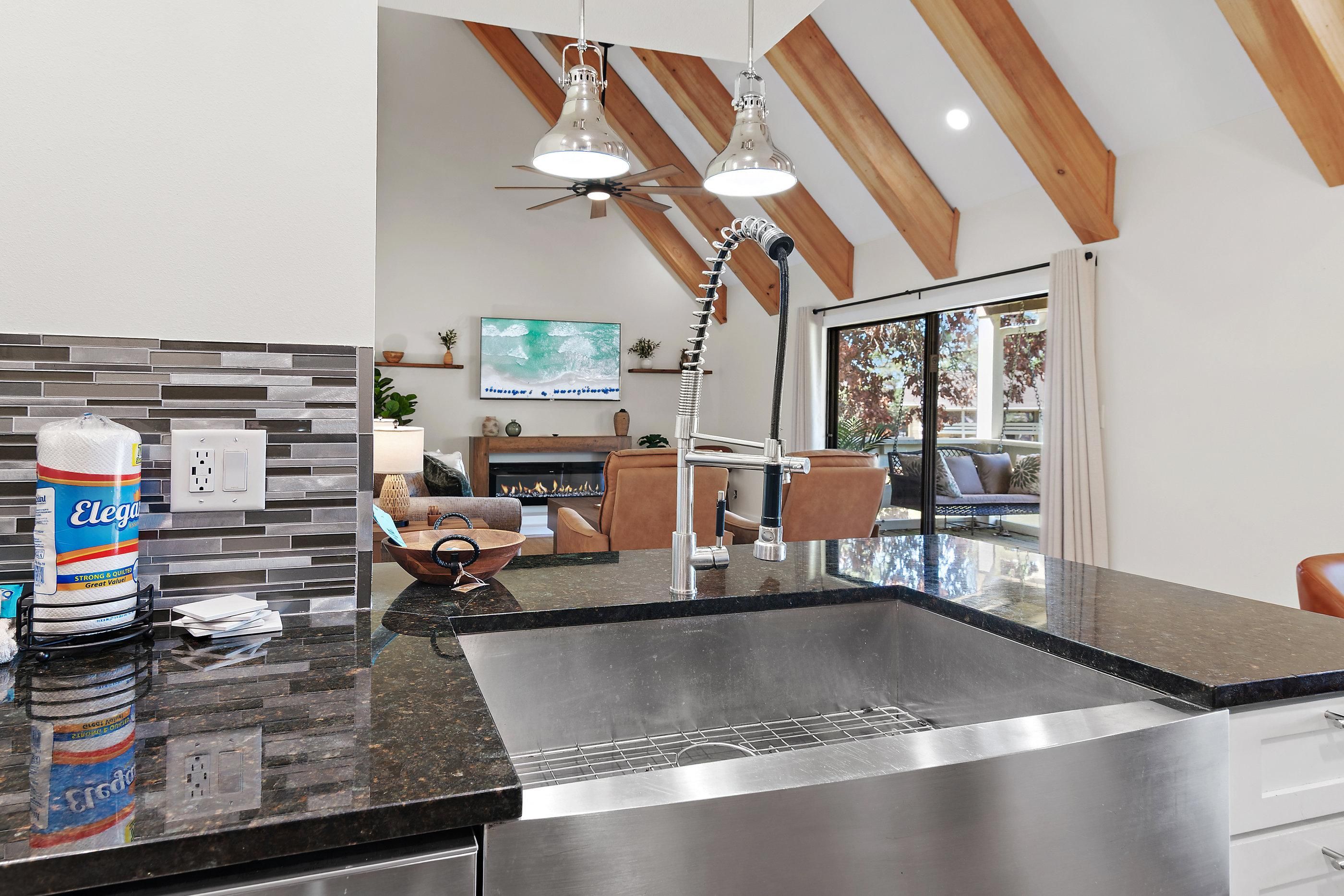 A modern kitchen with a granite countertop, stainless steel sink, and a ceiling fan.
