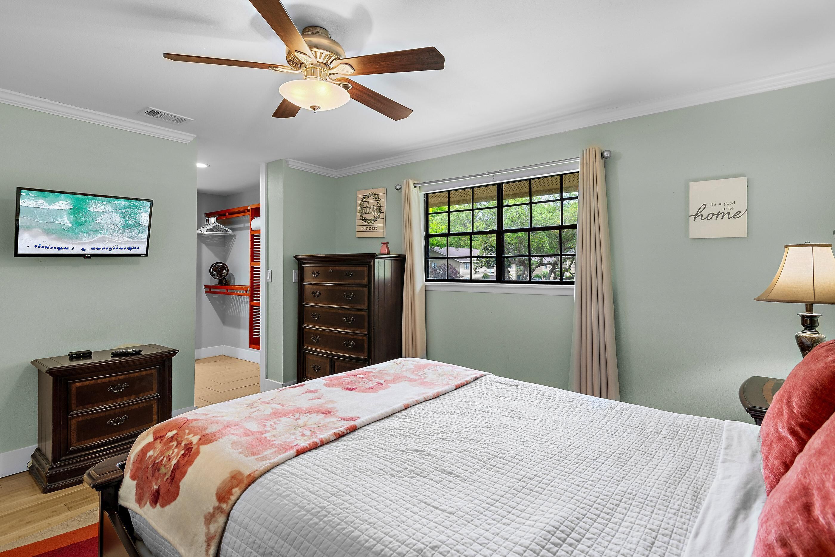 A bedroom with a bed, dresser, TV, window, and ceiling fan.
