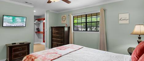 A bedroom with a bed, dresser, TV, window, and ceiling fan.