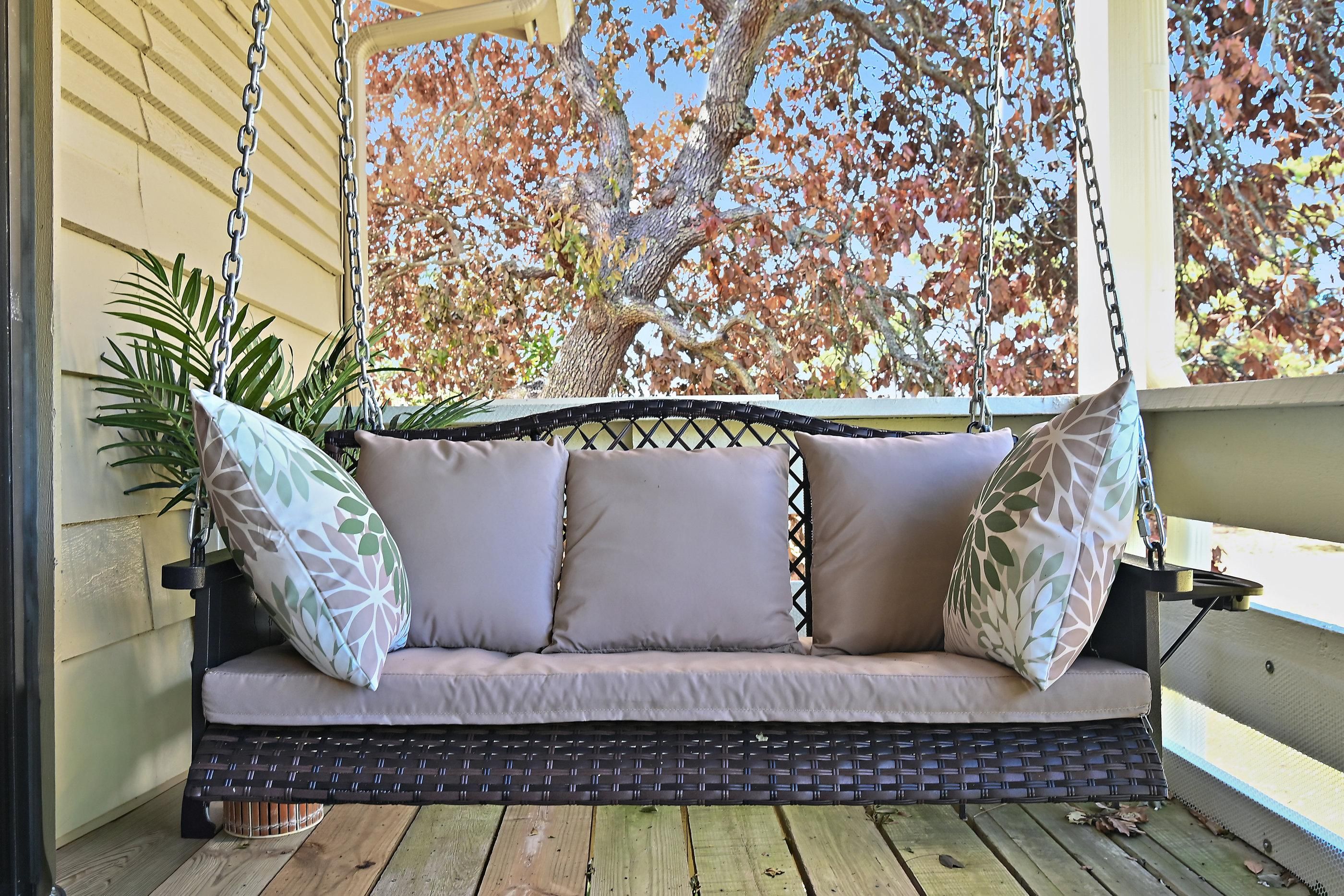 A porch swing with a cushioned seat and backrest, supported by metal chains and a woven base.