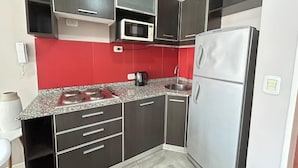A compact kitchen with dark cabinets, a microwave, a refrigerator, a granite countertop, and a red backsplash. - Marais Recoleta (Buenos Aires)