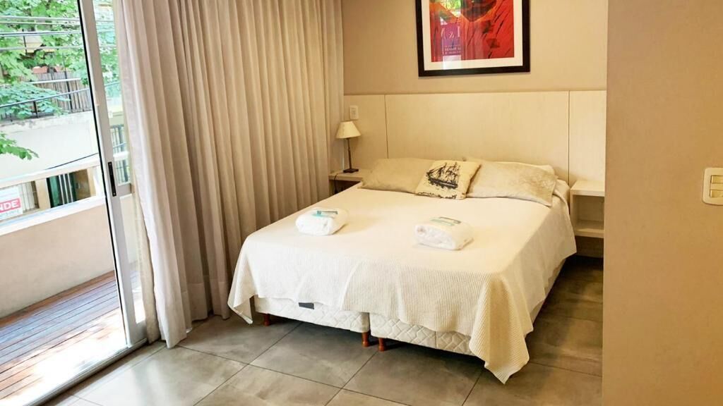 Een hotelkamer met een bed, een nachtkastje, een raam met gordijnen en een schilderij aan de muur.