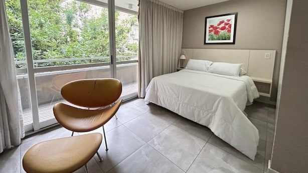 A hotel room with a bed, a chair, a window with curtains, and a framed picture on the wall. - Marais Recoleta (Buenos Aires)