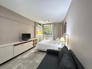 Una habitación de hotel moderna con una cama, televisor, sofá, escritorio y ventana con cortinas.