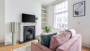 Een woonkamer met een open haard, een televisie, een bank en een raam met uitzicht.