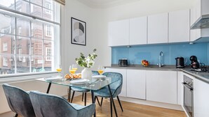 Een moderne keuken met witte kastjes, een blauw aanrecht en een eethoek met een glazen tafel en stoelen.