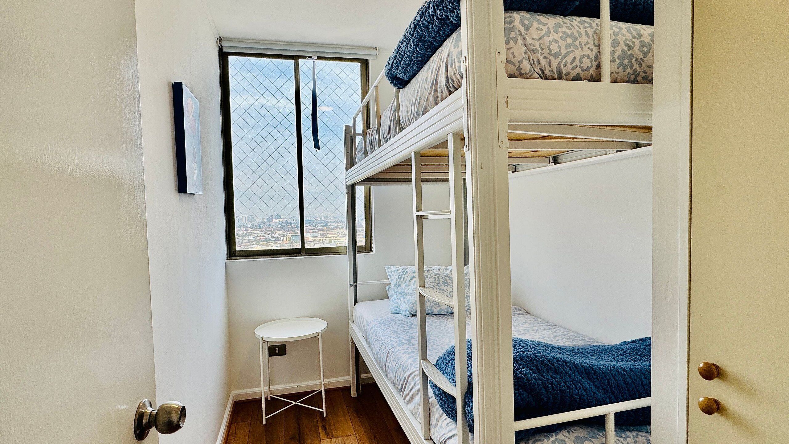Une chambre avec un lit superposé, une fenêtre, un petit tabouret et une porte.