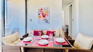 A dining area with wicker furniture, a table set for four, and a floral painting on the wall.