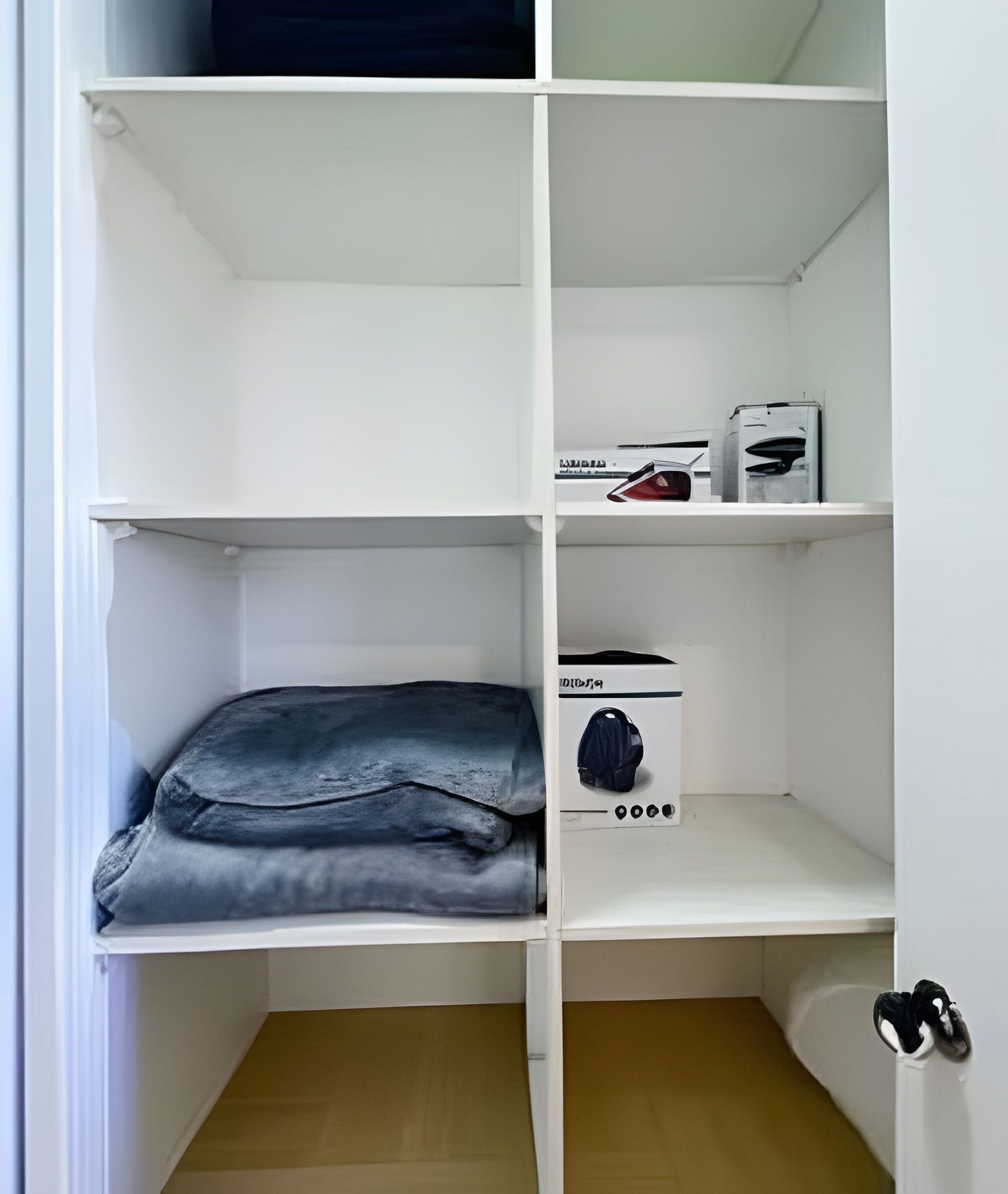 Un armario blanco con estantes, un objeto doblado en el estante inferior y una caja con tapa en el estante superior.
