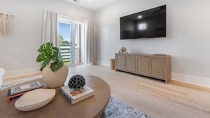A modern living room with a flat-screen TV, a large potted plant, a round wooden table, and a light-colored cabinet. - The Getaway, just blocks from the ocean. (Carolina Beach)