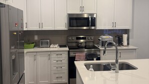 A modern kitchen with white cabinets, stainless steel appliances, and a central island with a sink. - Charming One‑Bedroom Getaway in a Peaceful Townhome Setting (Ottawa)
