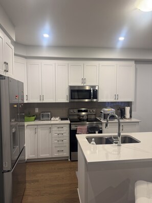 A modern kitchen with white cabinets, stainless steel appliances, and a central island with a sink. - Charming One‑Bedroom Getaway in a Peaceful Townhome Setting (Ottawa)