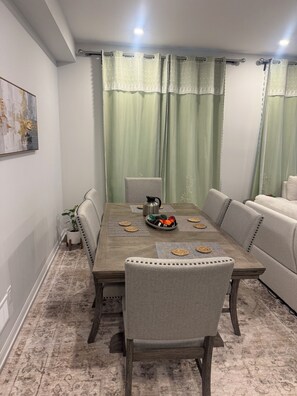 Un coin repas avec une table en bois, des chaises rembourrées, un bol décoratif et une plante en pot.