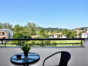 Ein Balkon mit Tisch und Stuhl, einem Blumentopf und Blick auf Häuser und Grünflächen.
