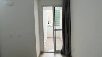A room with a bed, a door leading to a balcony, and a view of buildings outside.