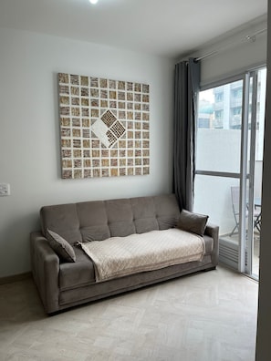 A modern living room with a sofa, a patterned wall art, and a sliding glass door leading to an outdoor area. - LK Centro 1 (Belo Horizonte)