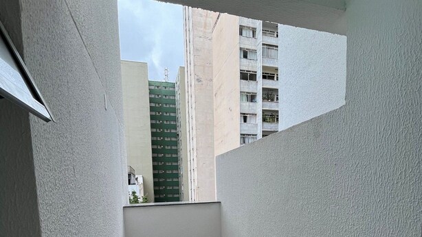 Un balcón pequeño y cerrado con suelo de baldosas y paredes lisas, con vistas a un edificio de varios pisos y balcones.