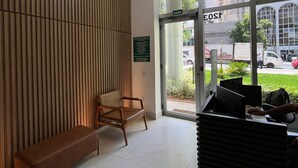 Zona de recepción con pared de paneles de madera, un banco, un mostrador con computadora y una puerta de vidrio que da al exterior.