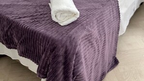 Una cama individual con una manta morada y una toalla blanca enrollada encima.