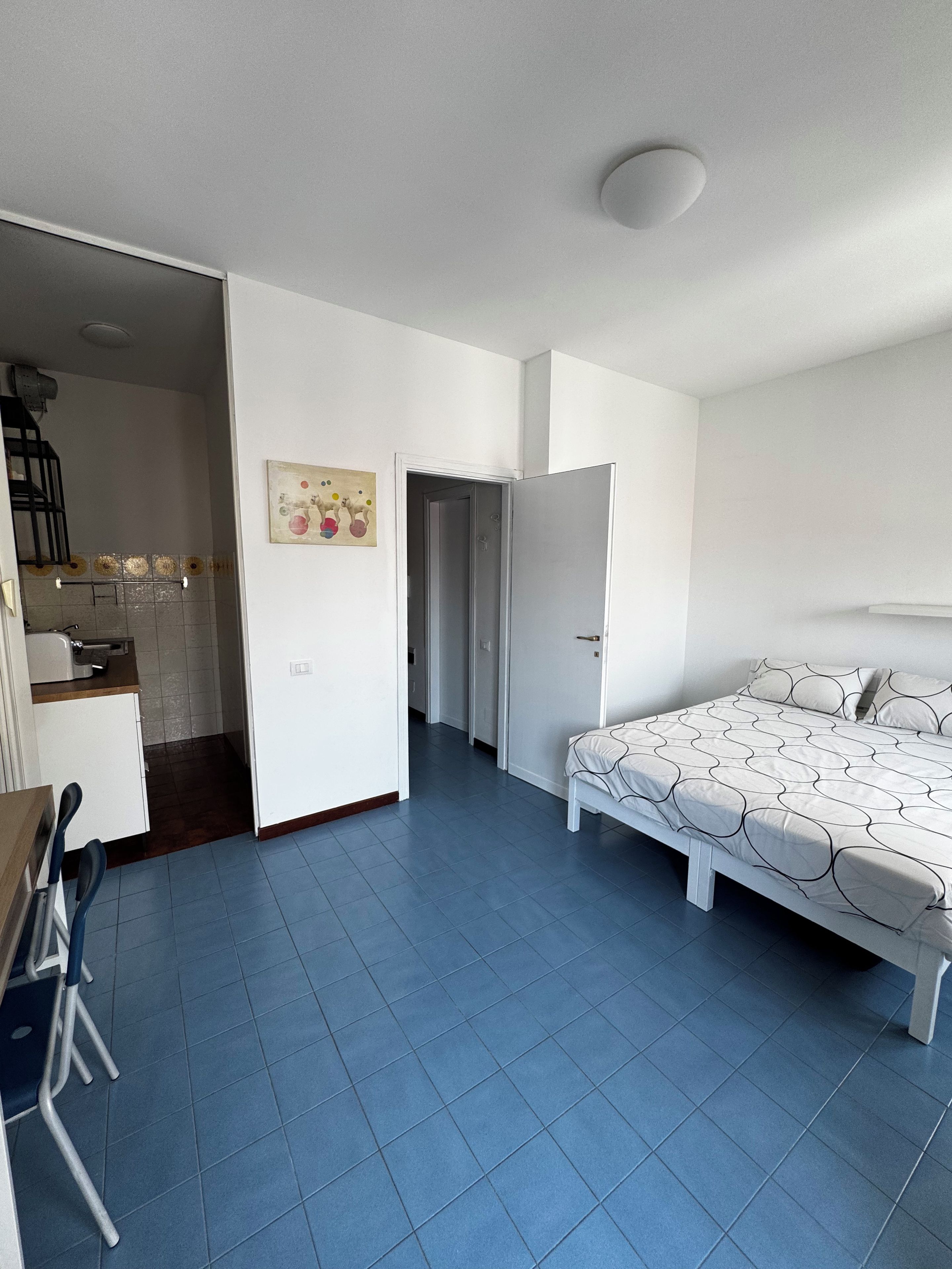 Une pièce comprenant un lit, un bureau et une chaise. Une porte donne accès à une autre pièce.