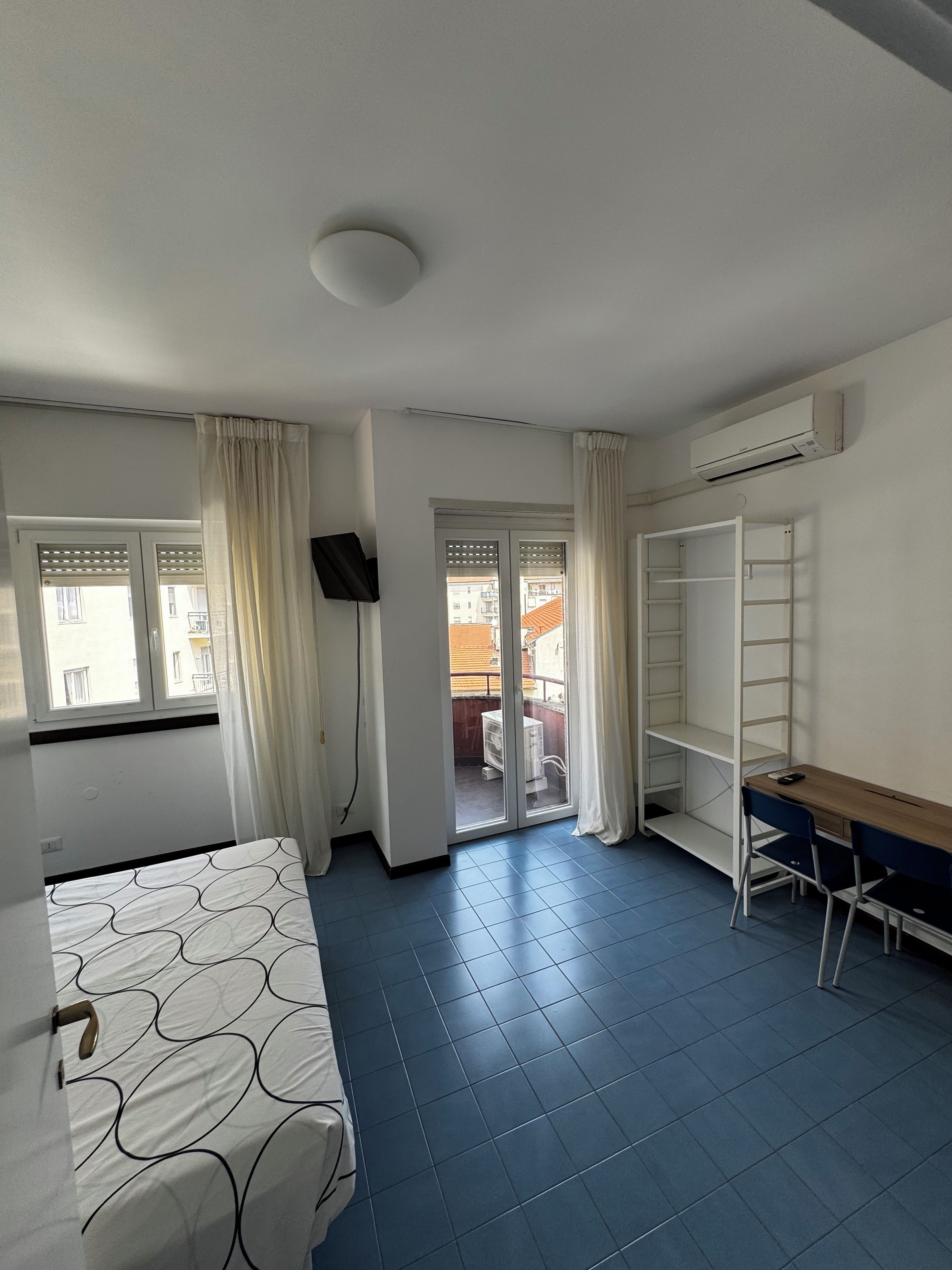 A hotel room with a bed, a desk, a wardrobe, and a television.