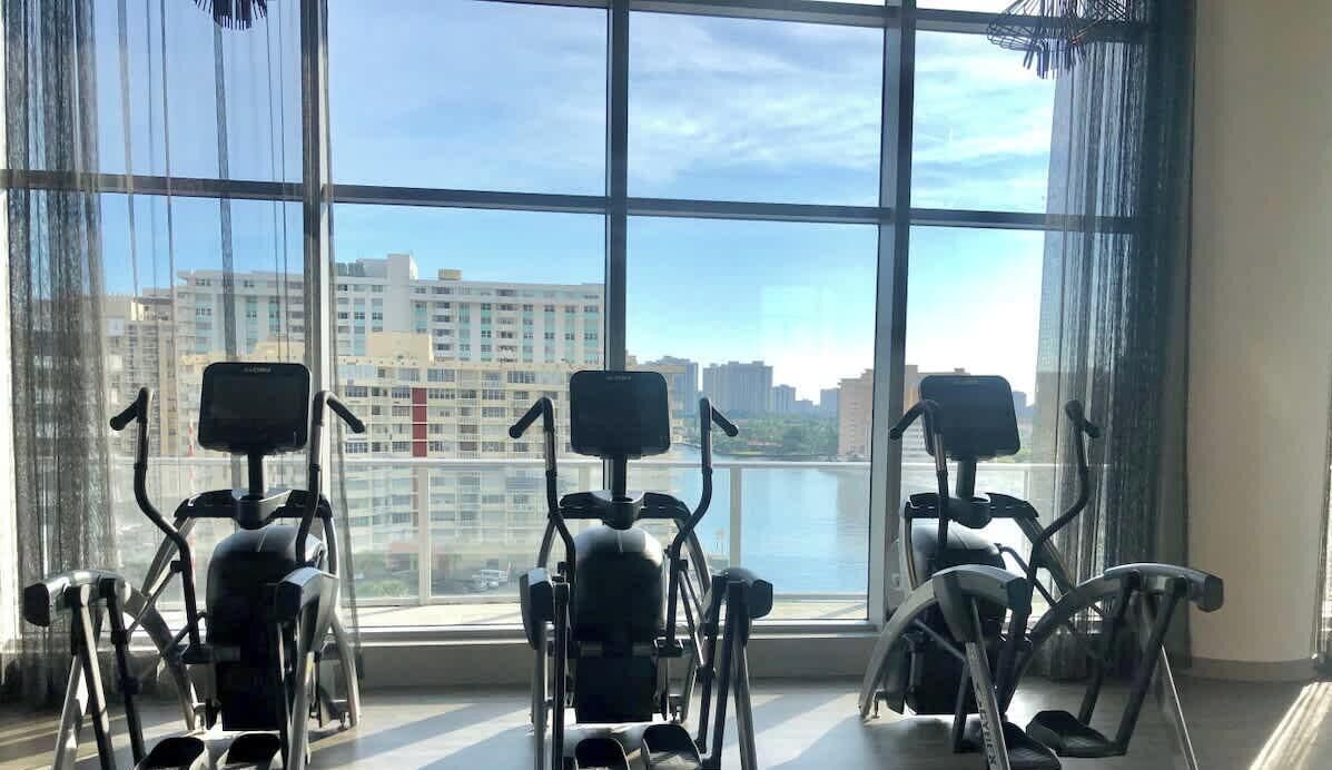 Trois vélos d’exercice sont installés dans une pièce dotée de grandes fenêtres donnant sur un paysage urbain.